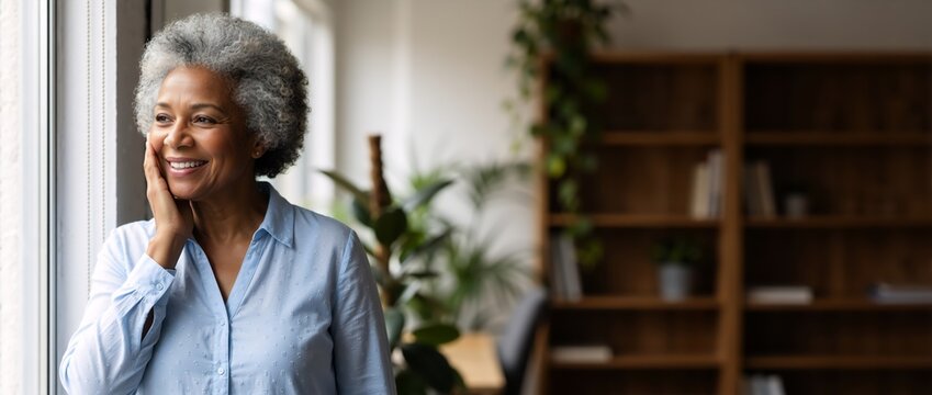 Happy senior african american woman smiling and looking out a window. Mature black lady enjoying a contented retirement lifestyle at home. Panoramic banner with copy space - Powered by Adobe