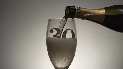 Glass engraved with the number 30. Champagne bottle fills the glass with alcohol. Celebrating milestone, anniversary or birthday