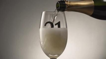 Glass engraved with the number 21. Champagne bottle fills the glass with alcohol. Celebrating milestone, anniversary or birthday