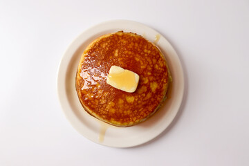 Pancakes with a pat of butter and syrup. Two thick pancakes are placed on a round plate.