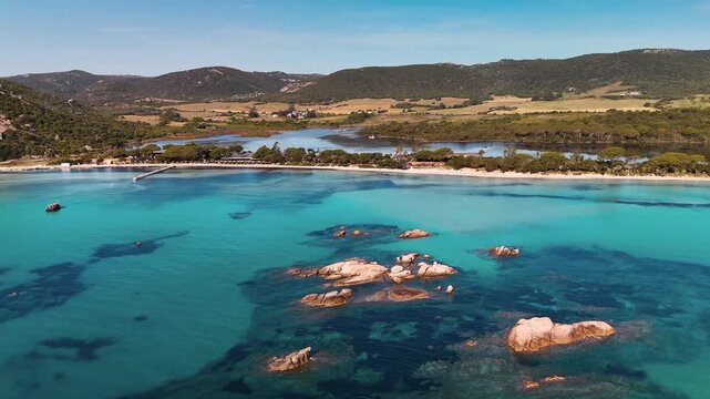Smooth Aerial Drone Zoom Out Shot Above Coastal Rocks, Revealing the Turquoise Lagoon and White Sand Beach of Plage de Santa Giulia, Porto Vecchio, Corsica, France.