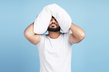 Man struggling with insomnia, covering head with pillow for quiet and rest