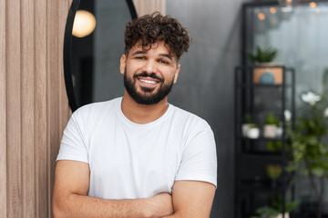 Smiling young man with curly hair and beard crossing arms, looking at camera