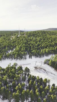 Drone flight parallel to a snowy mountain ski slope surrounded by dense pine forest, winter landscape, alpine terrain, ski resort infrastructure, peaceful nature, scenic aerial motion, winter tourism