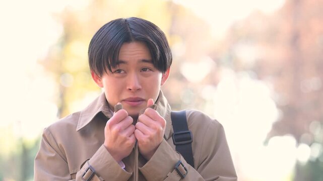 秋冬の紅葉の屋外で風邪をひいて寒気や悪寒、発熱や頭痛を感じるコートを着たビジネスマンの縦動画
