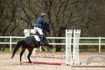 Equestrian man jumping obstacle with horse in riding arena