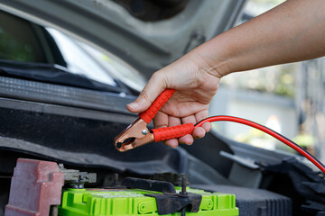 Hand holding jumper cable clamp near car battery