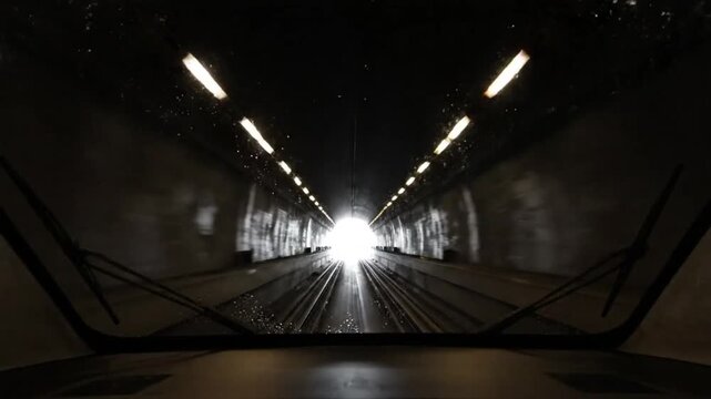 Traveling through a train tunnel with lights reflecting and windshield wipers clearing view