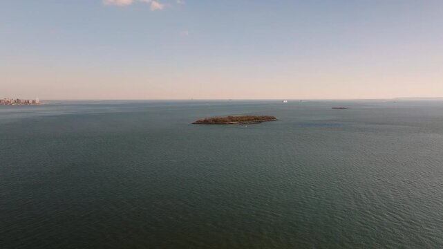 Aerial drone view of Hoffman Island in New York Harbor, a small historic island surrounded by calm open water with the distant coastline visible on the horizon.