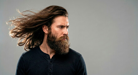 Serious bearded man with long blowing hair looking away on grey background
