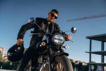 Against clear sky, in sunglasses. Man is outdoors with his motorcycle