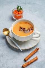 Sea buckthorn herbal tea in a cup on a light background with spices, berries and spoon.