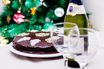 Chocolate cake with sprinkles, champagne bottle, and glasses near Christmas tree