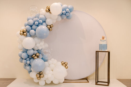 Trendy photo wall or zone decoration white, blue, gold balloons in hall restaurant. Celebration baptism concept. Delicious reception at birthday party. Cake on background decor for baby boy.