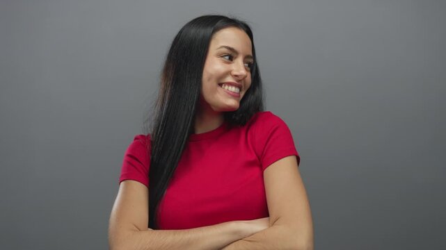 Woman smiling with arms crossed in red shirt against a grey background conveying confidence and happiness.