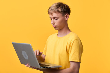 Laptop use by focused man in a yellow tee, studying and coding in a bright studio, showcasing modern technology, online work, and learning with a sleek digital setup