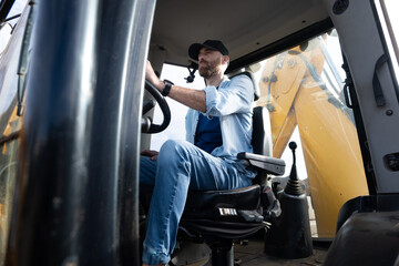Young man driving a backhoe loader in the countryside