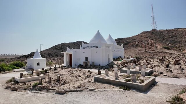 Mirbat cemetery in Southern Oman featuring historical white tombs and mausoleums on a dry hill next to the Arabian Sea, showing traditional Islamic burial structures of Oman in Mirbat town