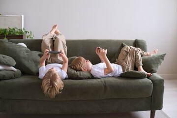 kids boys twins using smartphones lying on the couch