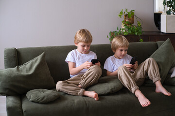 kids blonde boys twins using smartphones on the couch in living room