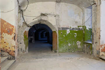 Abandoned prison corridor with arched tunnel entrance and peeling green paint walls, derelict jail hallway interior with deteriorating plaster and exposed brick, old correctional facility passage