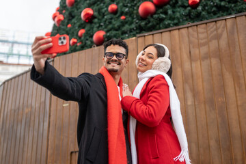 Smiling couple taking christmas selfie with smartphone in madrid, celebrating holiday season