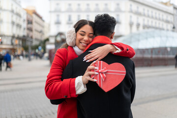 Cheerful young woman hugging her partner, receiving a heart-shaped gift box. Sharing a romantic...