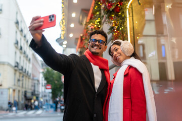 Happy diverse couple taking a selfie on a city street during christmas, enjoying winter holidays in madrid