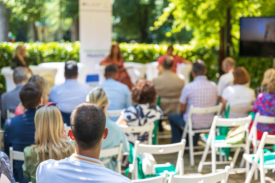 Outdoor business conference with professional audience attending presentation in green garden venue under canopy, sustainable corporate event setting
