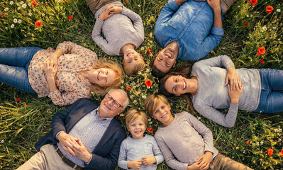 Happy family lying in circle on grass top view