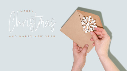 Merry Christmas and Happy New Year Greeting Card With Hands Holding Craft Envelope And White Snowflake On Soft Pastel Background. Perfect For Winter Holiday Cards And Elegant Seasonal Campaigns
