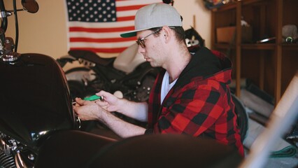 Mechanic working on a motorcycle in a garage while an American flag hangs in the background during a bright afternoon