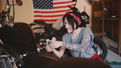 Mechanic female works on motorcycle in garage adorned with flag showcasing American spirit and personal passion for bikes