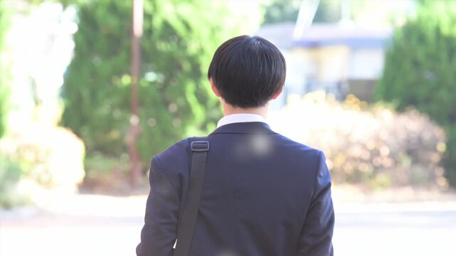 桜吹雪の逆光の美しい新緑や緑の背景でビジネススーツを着た笑顔の歩く新卒の学生や営業男性の使いやすいスローモーション動画　顔無しの後ろ姿