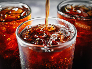 Cola soft drink with ice cubes, soda fizzy drink in Cold three glass on gray background, close-up