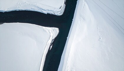 Aerial view of a winding dark river flowing through a vast pristine white snow and ice landscape during winter