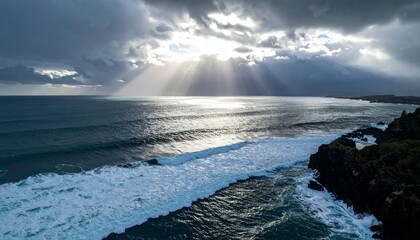Dramatic ocean waves crash on a rugged dark rocky coastline under a stormy sky with sun rays breaking through