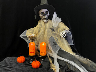 halloween witch with pumpkin. Halloween decoration with two orange LED candles in black holders, small pumpkins, and plastic spiders on a dark background with blue lighting and cobwebs