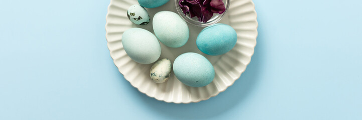 A plate holds several blue-painted Easter eggs and a couple of small patterned eggs, creating a festive atmosphere for the holiday celebration, small bowl of red cabbage, how to dye eggs blue, banner