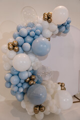 Trendy photo wall or zone decoration white, blue, gold balloons in hall restaurant. Balloons. Decor closeup on arch. Celebration baptism concept. Birthday decor for baby boy party.