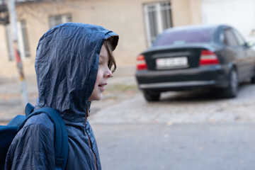 Profile of a young boy in a hooded jacket with a backpack. Child walking to school outdoors