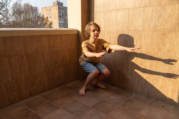 Young boy doing squat exercises on a balcony. Child's home workout for fitness and health