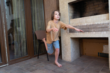Active young boy balancing on one leg at home. Child doing fitness exercise on a patio