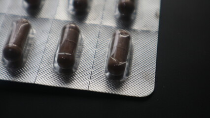 Brown Medical Capsules in Blister Pack on Dark Background.