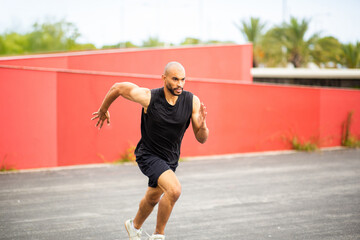 Focused male with shaved hair and beard athlete sprinting on city track