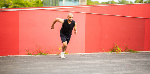 Focused athlete in black outfit sprinting past red urban wall