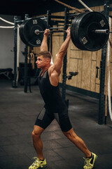 View from the side. Athletic man performing weightlifting exercises with a barbell in a gym