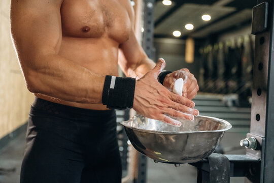 Fitness man is rubbing his hands with chalk, specifically magnesium carbonate