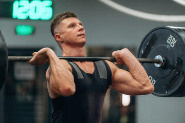 Workout session. Athletic man performing weightlifting exercises with a barbell in a gym