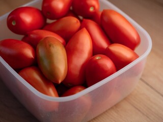 Plastic container full of red tomatoes on a wooden table.